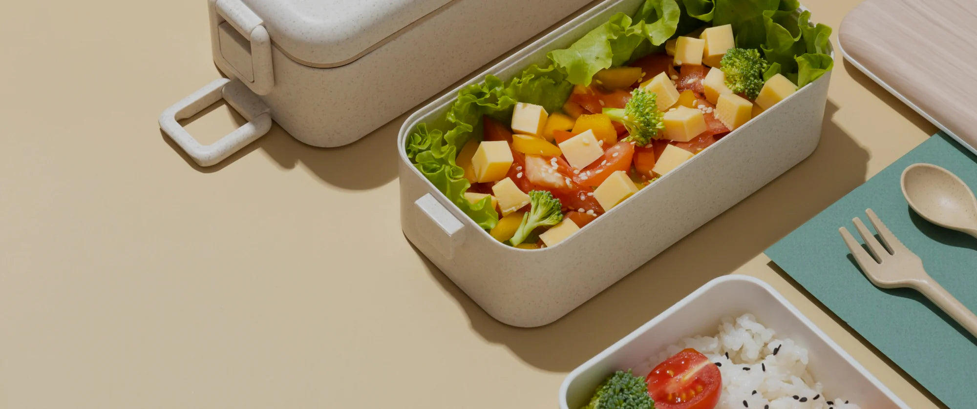 Bento box with salad and other food items on a beige surface